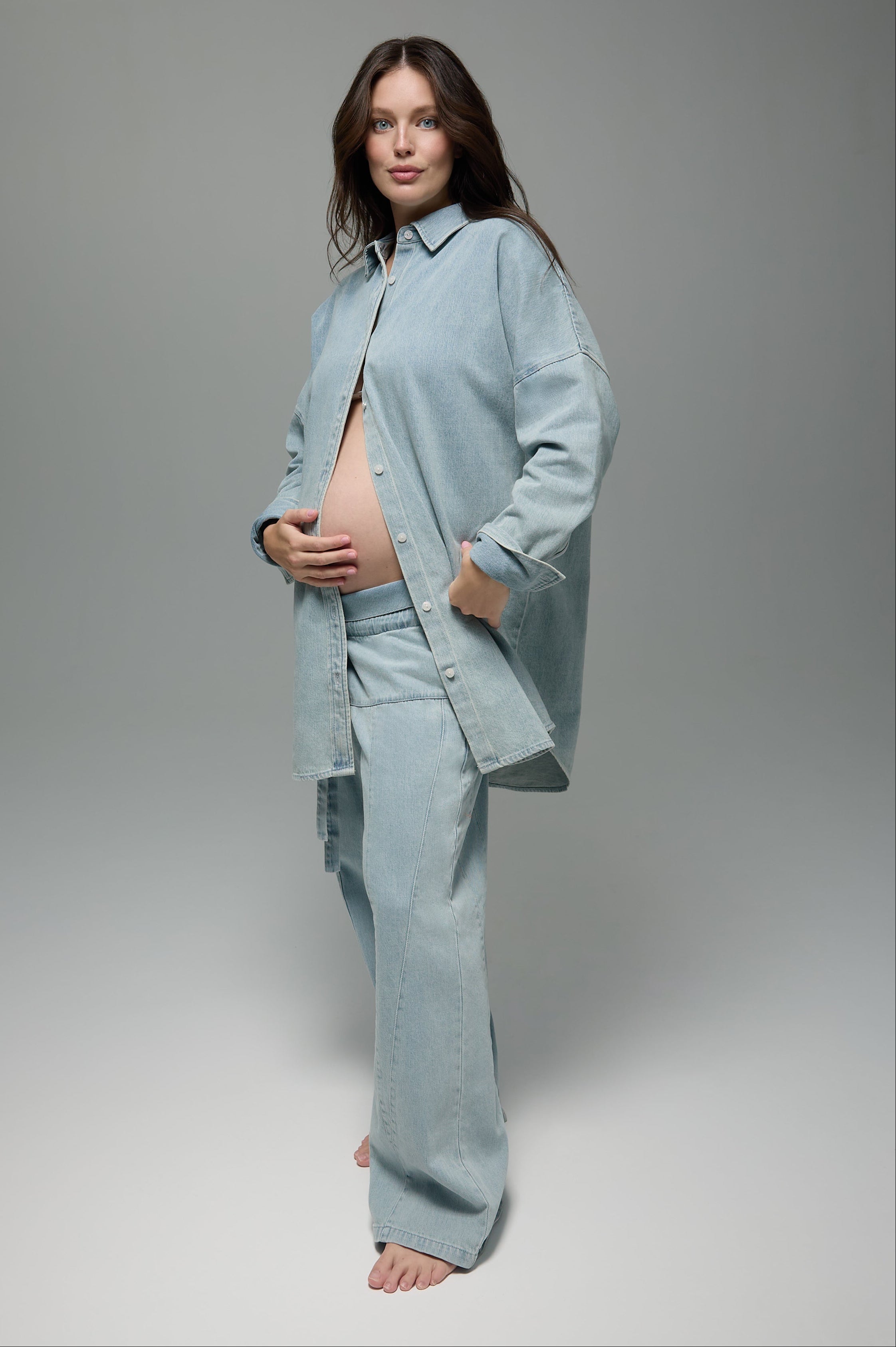 Pregnant woman wearing a light blue denim outfit on a gray background