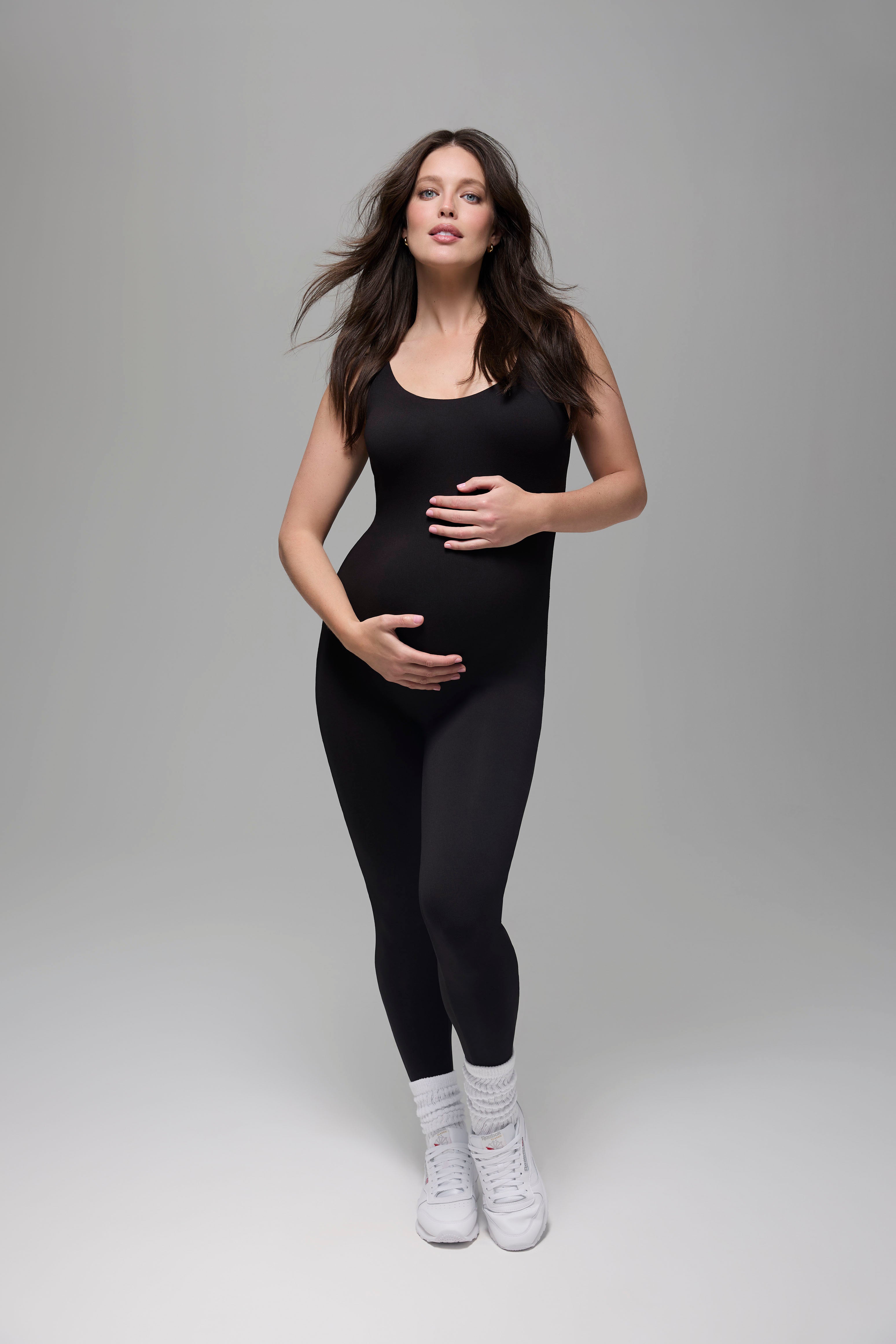 Pregnant woman wearing a black Bumspuit outfit on a grey background
