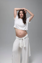 Pregnant woman wearing a white sleep outfit by Bumpsuit against a gray background