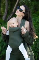 woman with a baby in the bumpsuit forest green baby carrier in nature