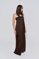 Pregnant woman wearing a Bumpsuit brushed satin gown in a chocolate color against a white background