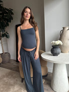 Pregnant woman wearing a Bumpsuit cloud cement blue tank top and pants in a living room.