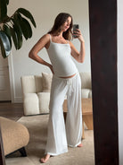 Pregnant woman taking a mirror selfie wearing a Bumpsuit cloud ivory tank top and pants in a living room.