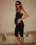 Pregnant woman wearing a black Bumpsuit camisole tank top and capri leggings against a beige wall