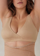 Woman wearing a beige reversible comfy bra in beige against a plain background