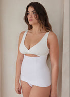 Woman wearing a white reversible comfy bra and support waist trainer against a beige wall