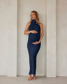 pregnant woman wearing a turtleneck dress in navy against a beige feature wall