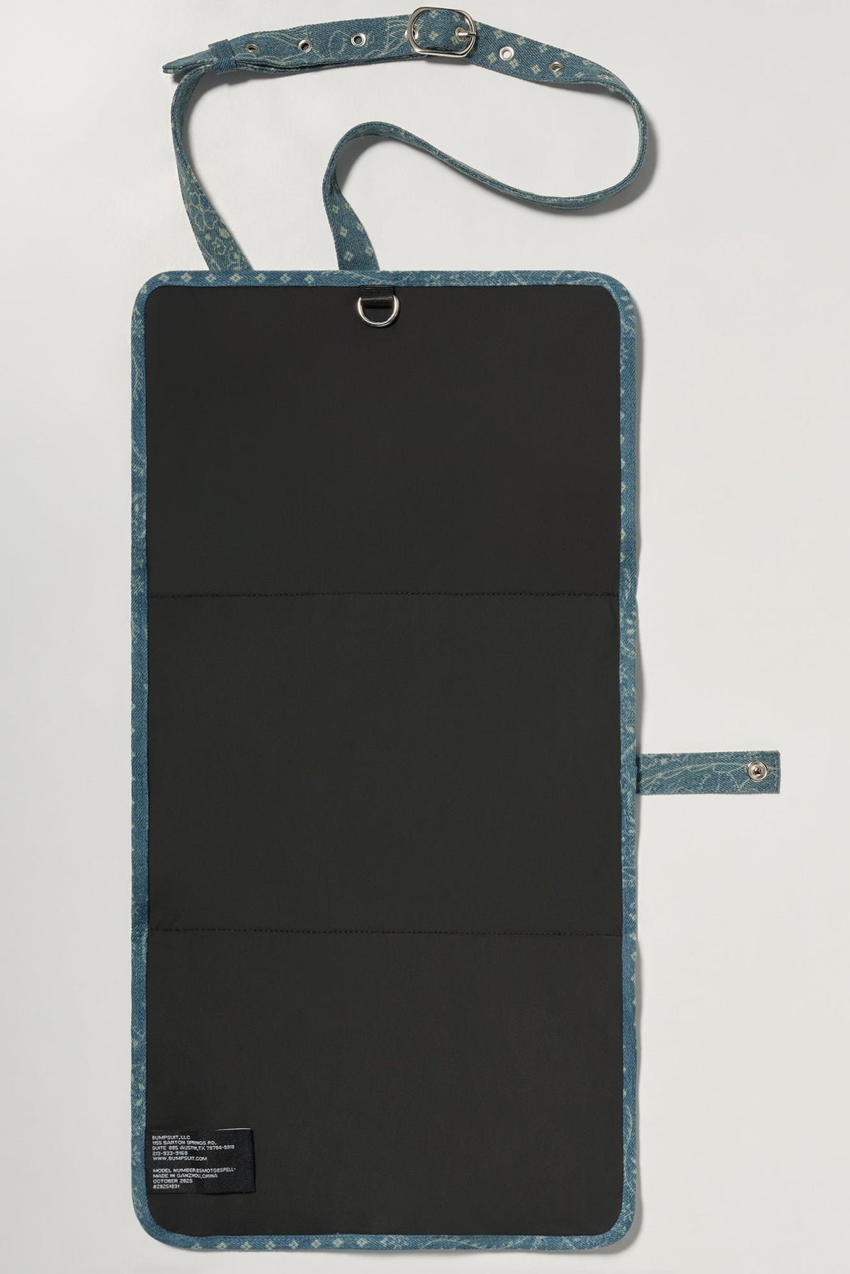 Open view of Mom-On-The-Go Bag showcasing black changing mat and denim shoulder strap on light gray background