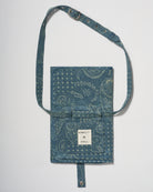 A blue denim crossbody diaper change mat bag by with a paisley and geometric pattern by Spell and Bumpsuit,, shown on a light gray background.