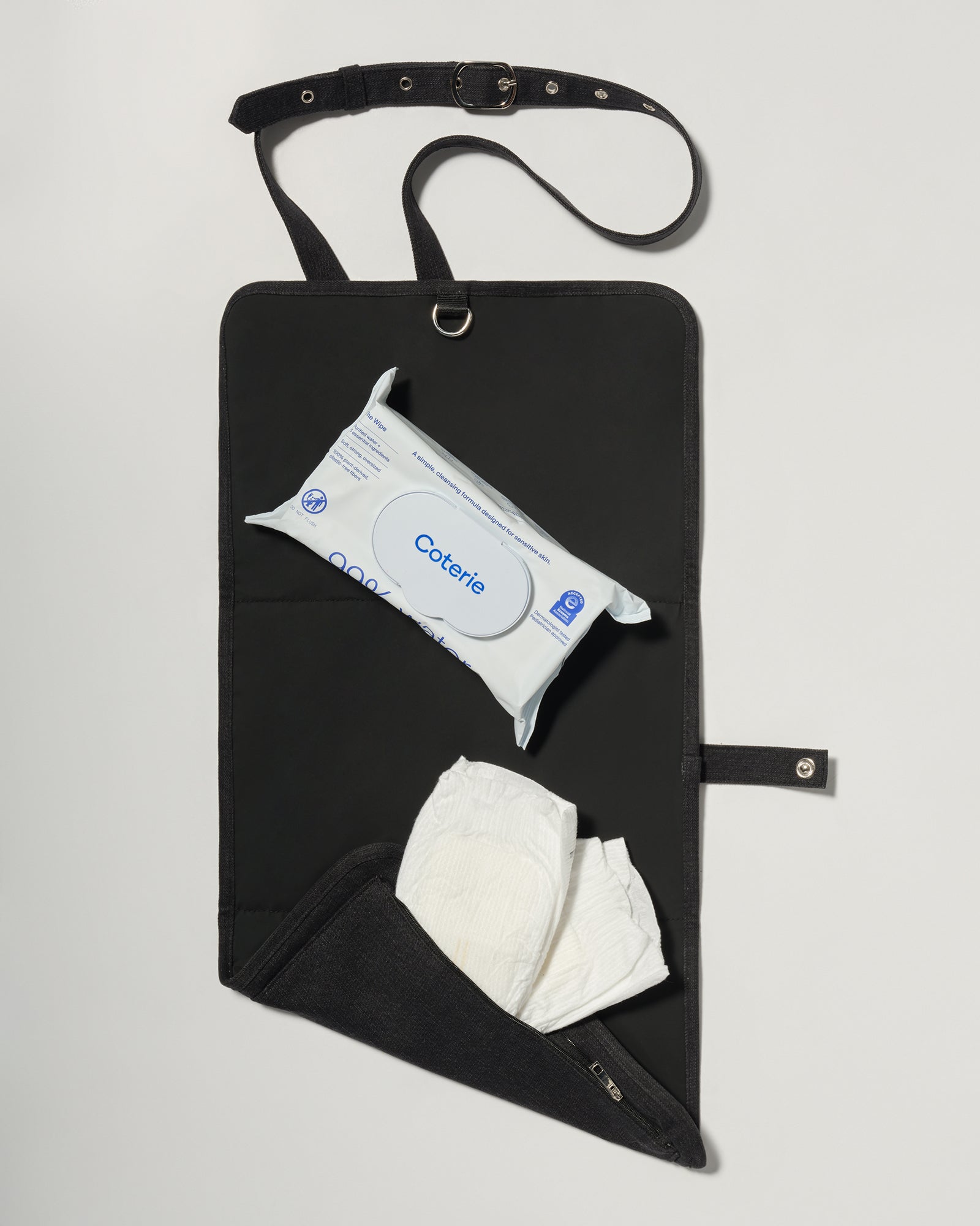 A black fabric diaper bag or organizer pouch with a top strap, shown on a light gray background. The pouch has a front pocket holding a package of baby wipes and a white diaper hanging below.