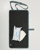 A denim roll up diaper change mat bag by Spell and Bumpsuit with a black inside lining, shown on a light gray background with wipes and diapers