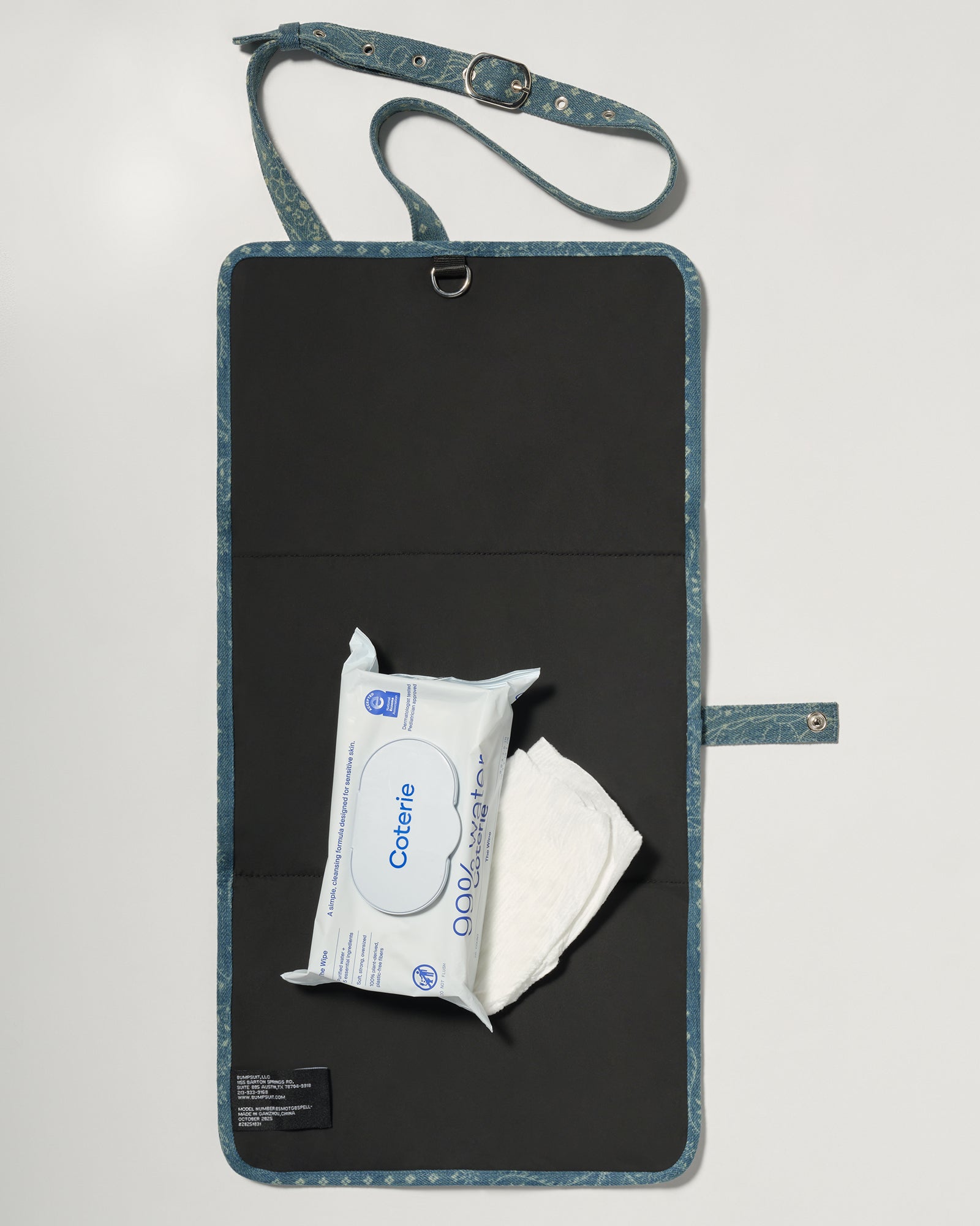 A denim roll up diaper change mat bag by Spell and Bumpsuit with a black inside lining, shown on a light gray background with wipes and diapers
