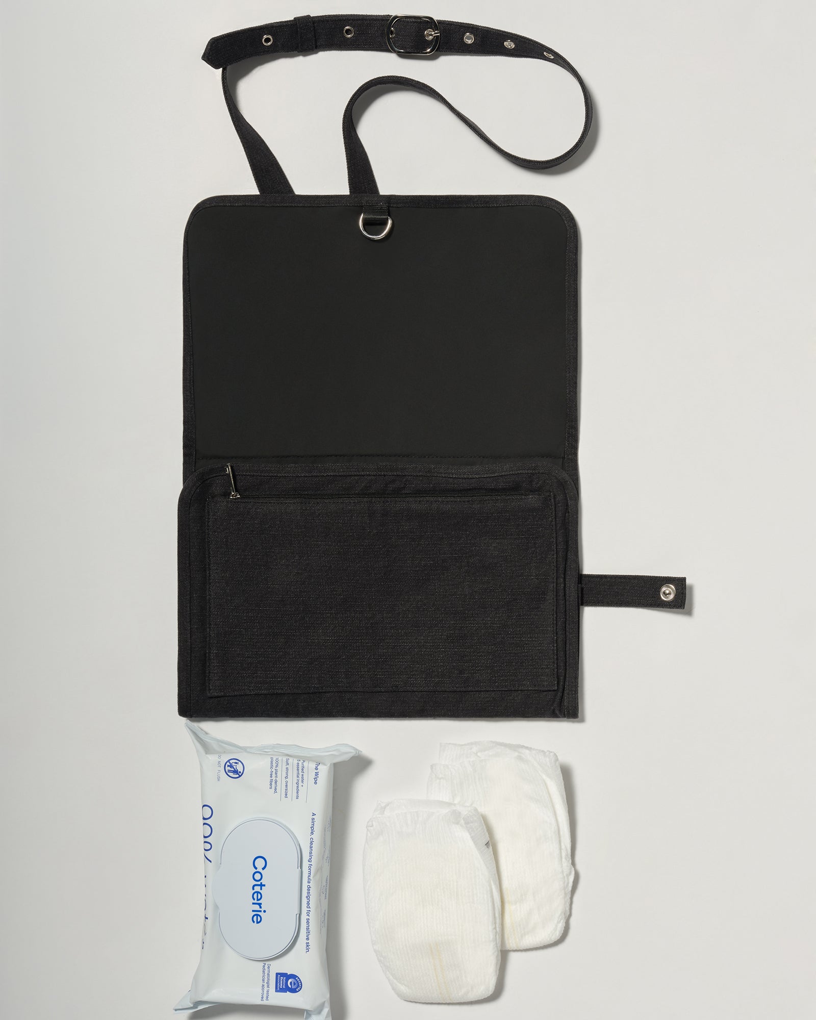 A black denim roll up diaper change mat bag by Spell and Bumpsuit,, shown on a light gray background with wipes and diapers