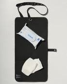 A black denim roll up diaper change mat bag by Spell and Bumpsuit,, shown on a light gray background with wipes and diapers