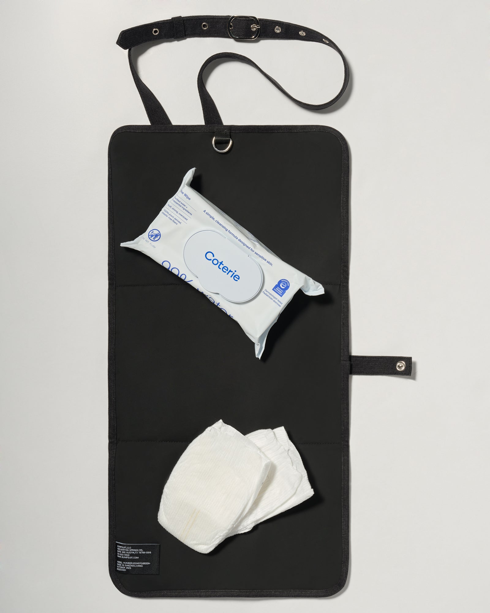 A black denim roll up diaper change mat bag by Spell and Bumpsuit,, shown on a light gray background with wipes and diapers
