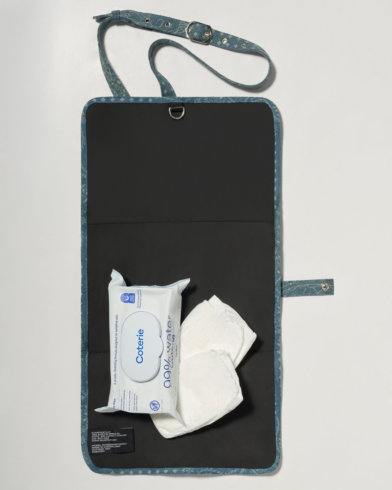 A black denim roll up diaper change mat bag by Spell and Bumpsuit,, shown on a light gray background with wipes and diapers