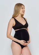 Pregnant woman wearing th Bumpsuit black maternity reversible comfy bra against a plain background