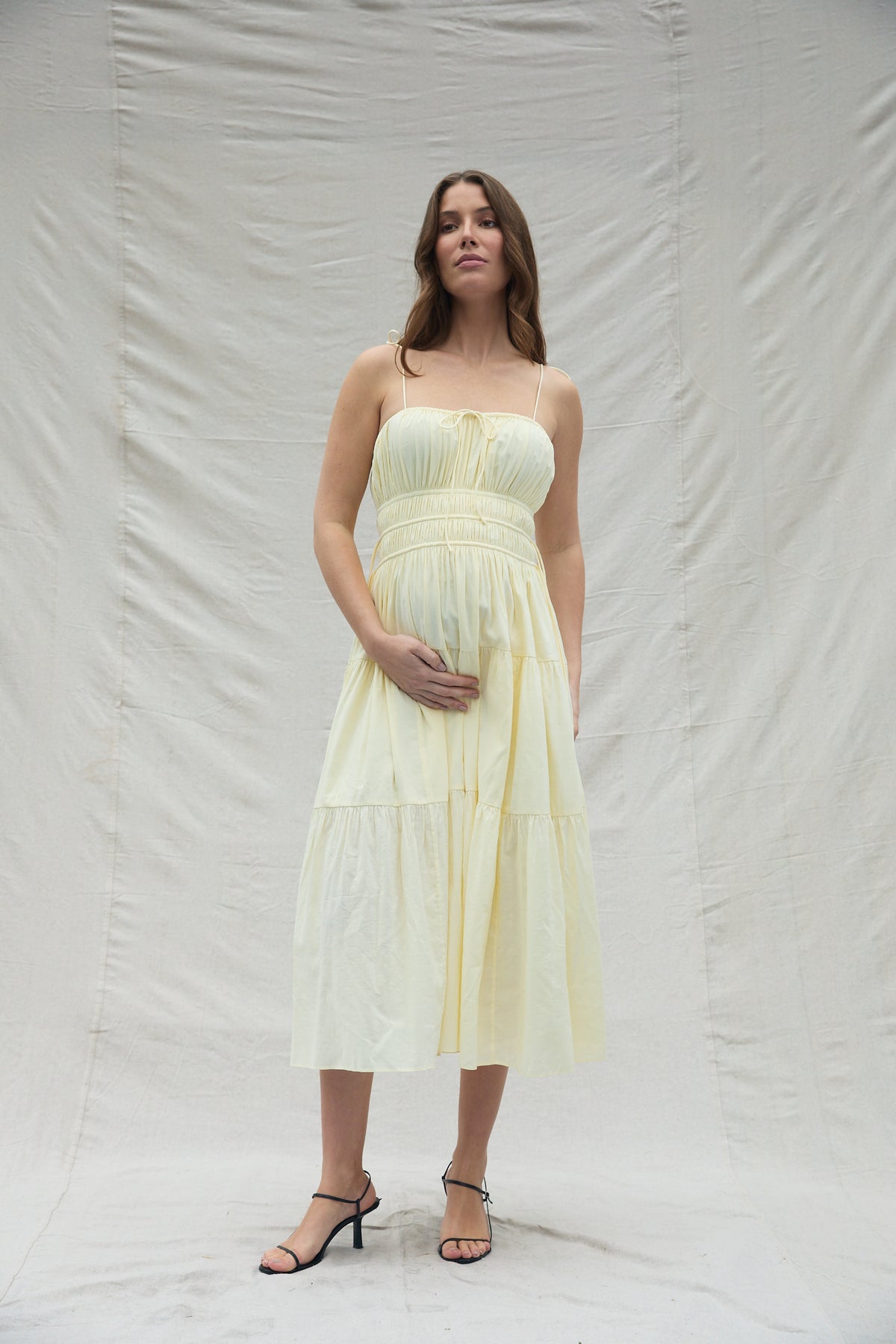 Woman wearing a shirred midi flowing yellow dress against a plain background