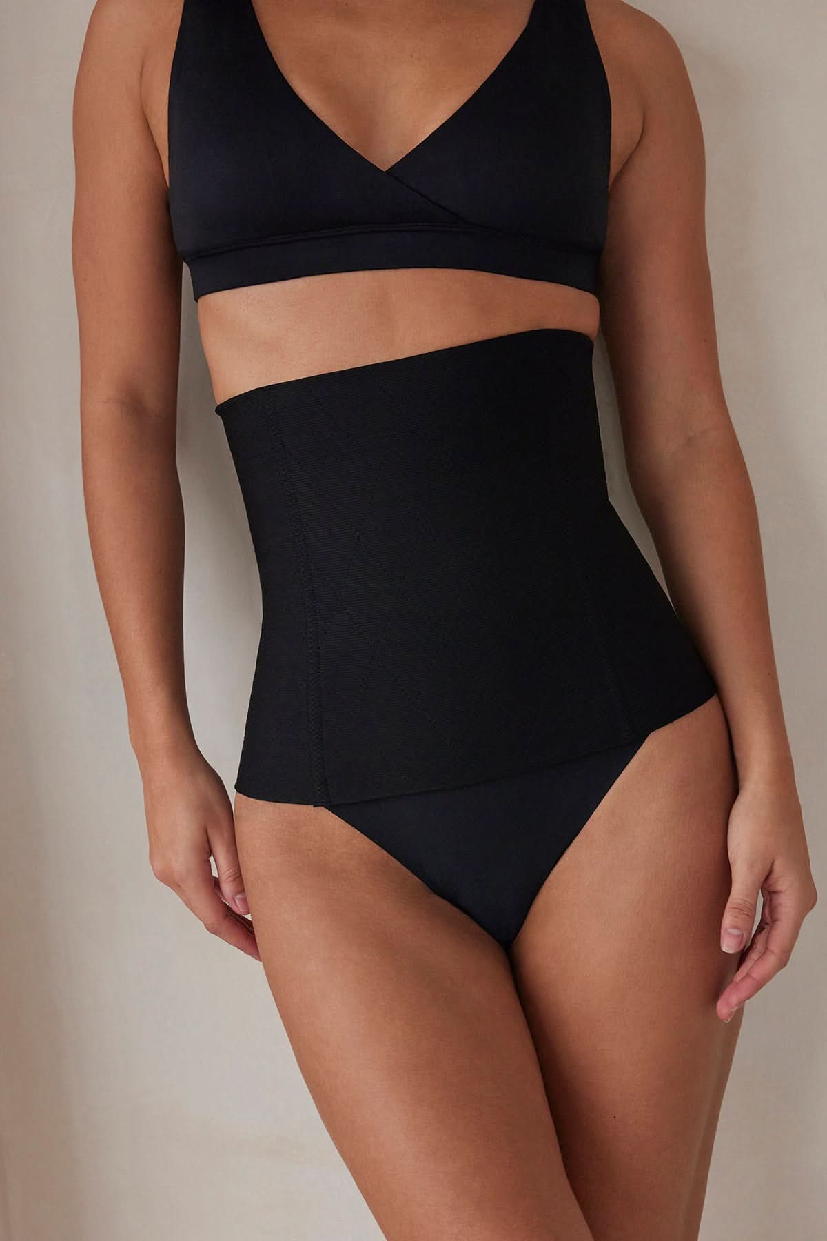 Woman wearing the postpartum support waist trainer in black by bumpsuit