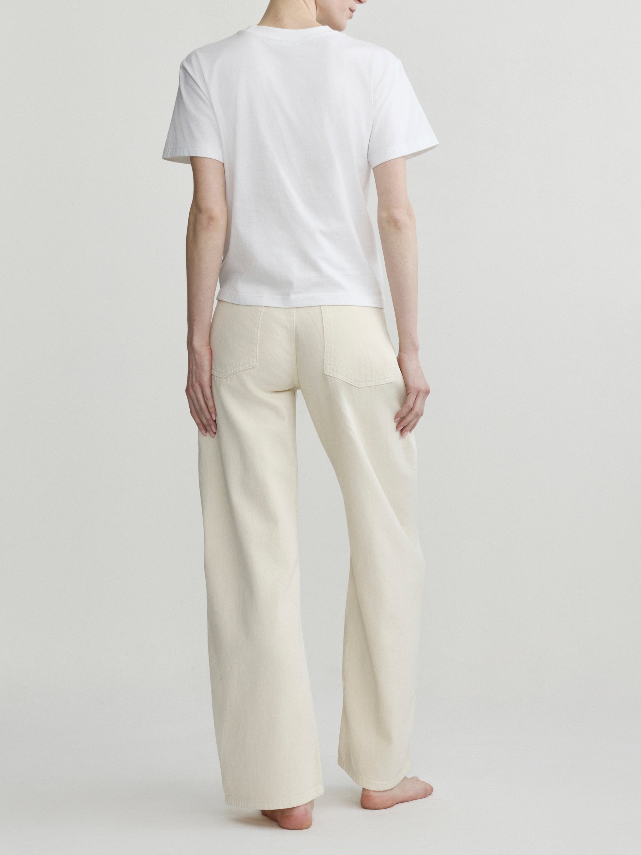 Back view of a person wearing a white t-shirt and beige pants on a plain background
