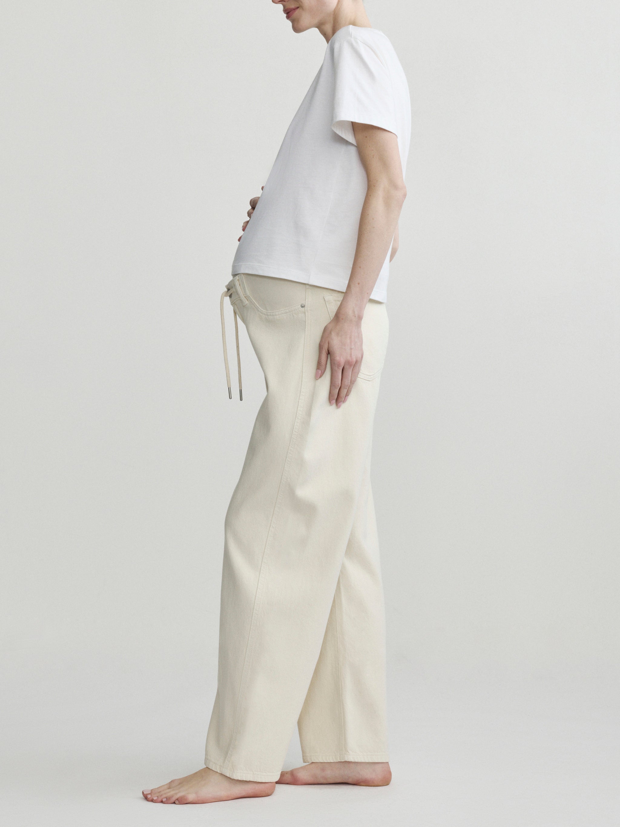 Pregnant person wearing a white t-shirt and beige pants on a plain background