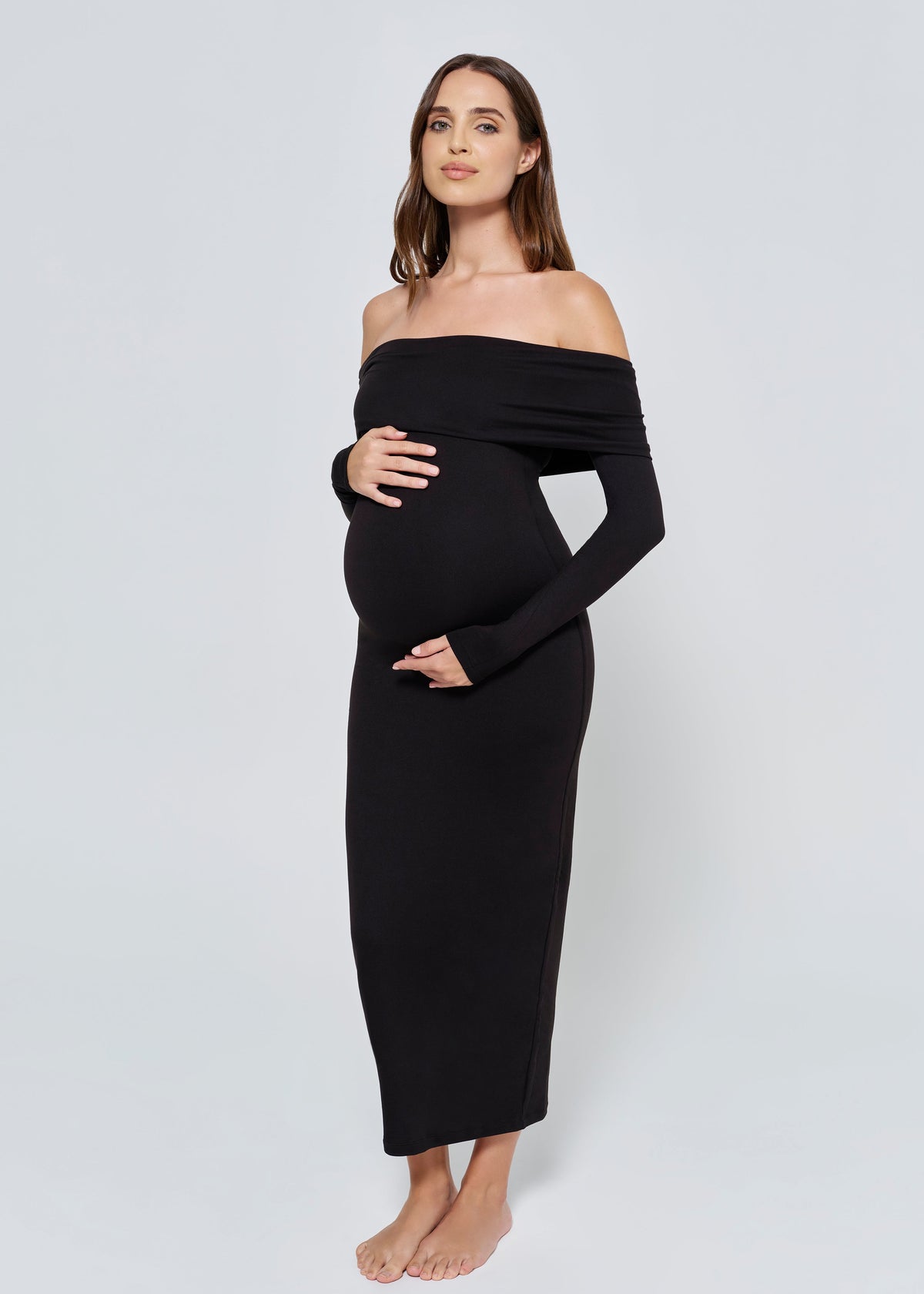 Pregnant woman wearing a black off-shoulder dress against a white background