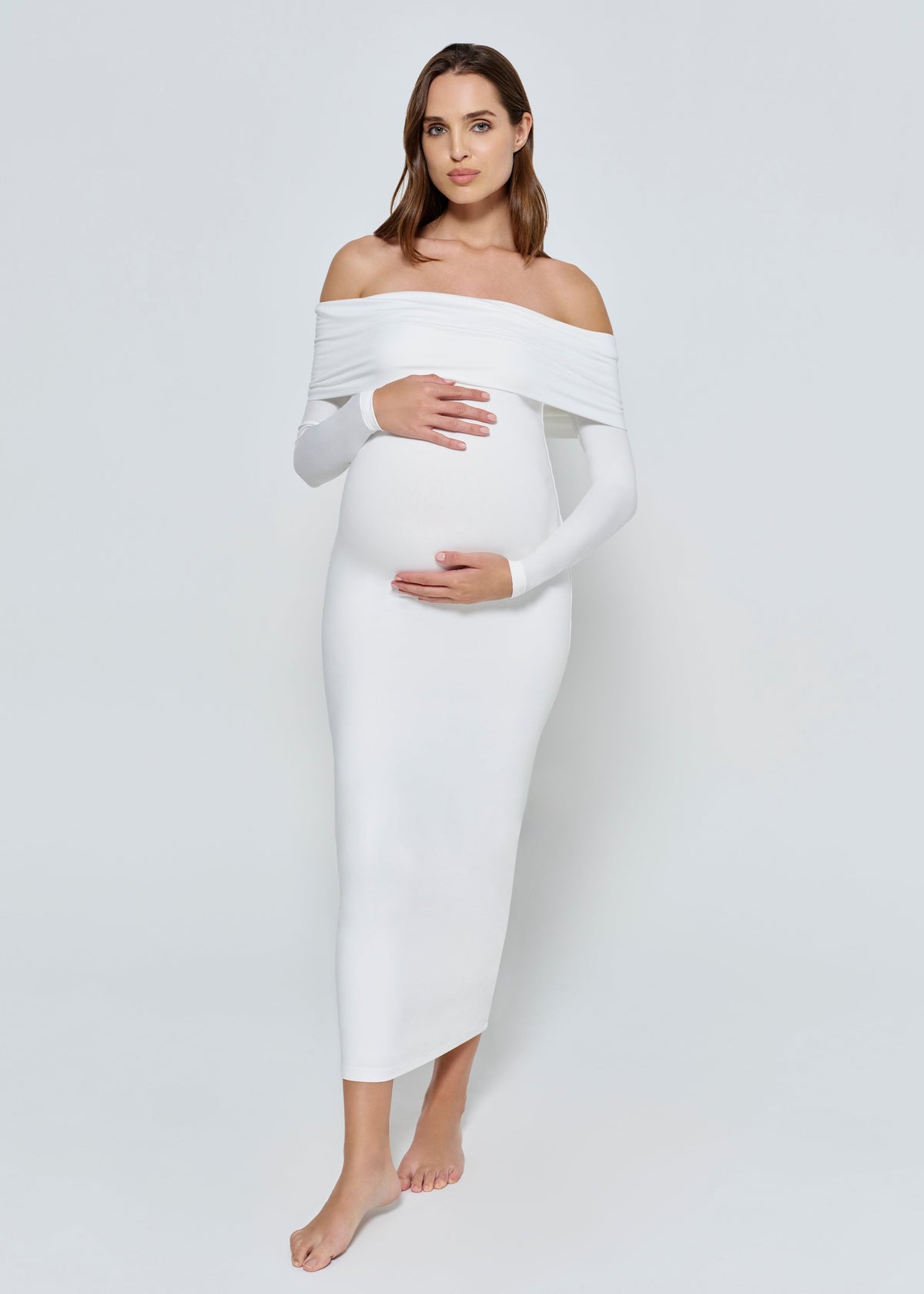 Pregnant woman wearing a ivory off-shoulder dress against a white background