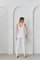 Woman wearing a light grey Bumpsuit standing in front of a minimalist background with arches.