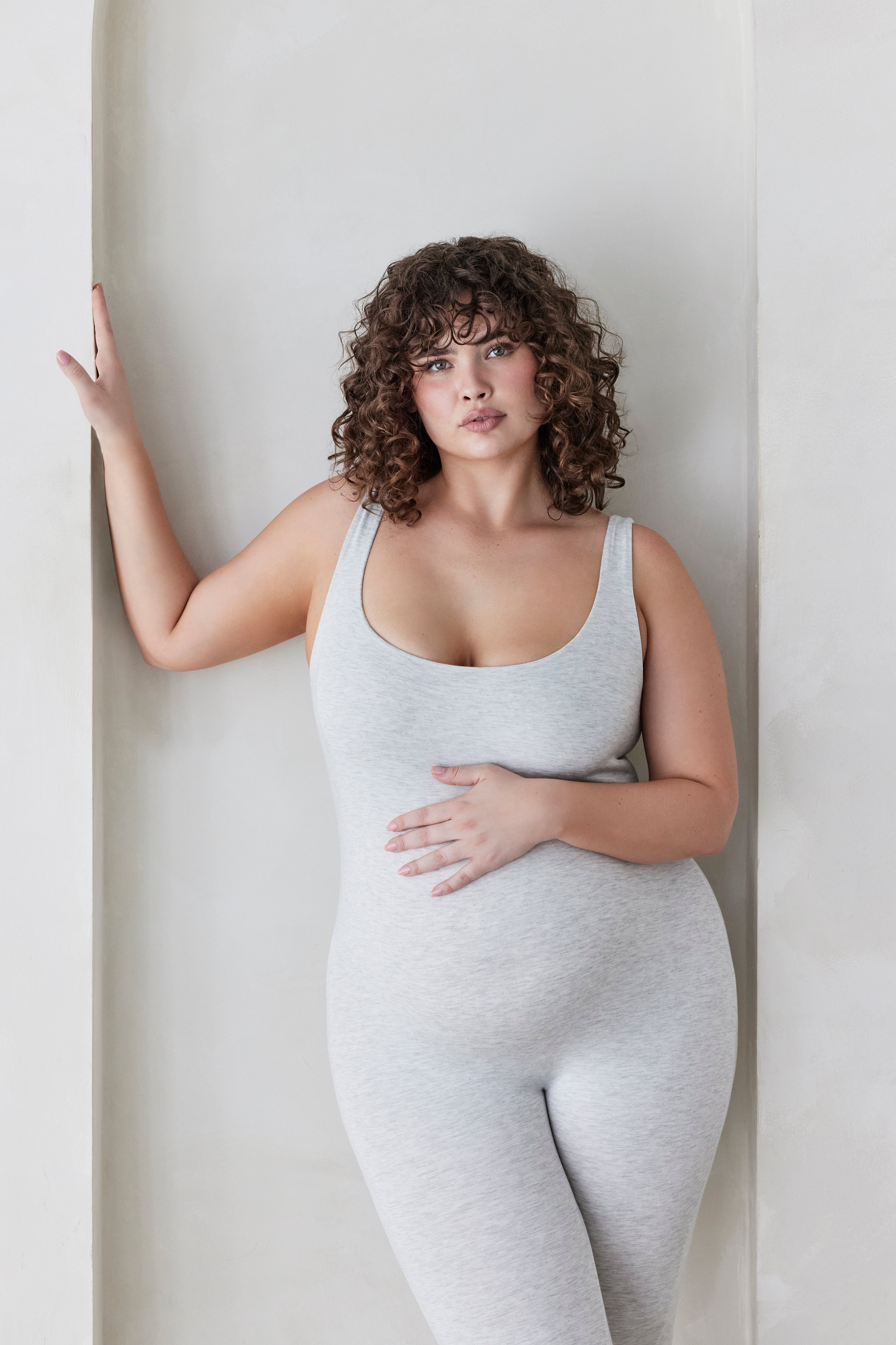 Woman wearing a light grey Bumpsuit against a white wall