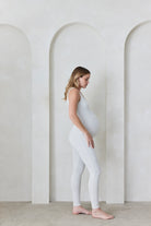 Pregnant woman wearing a heather grey Bumpsuit in a minimalistic setting with arches.