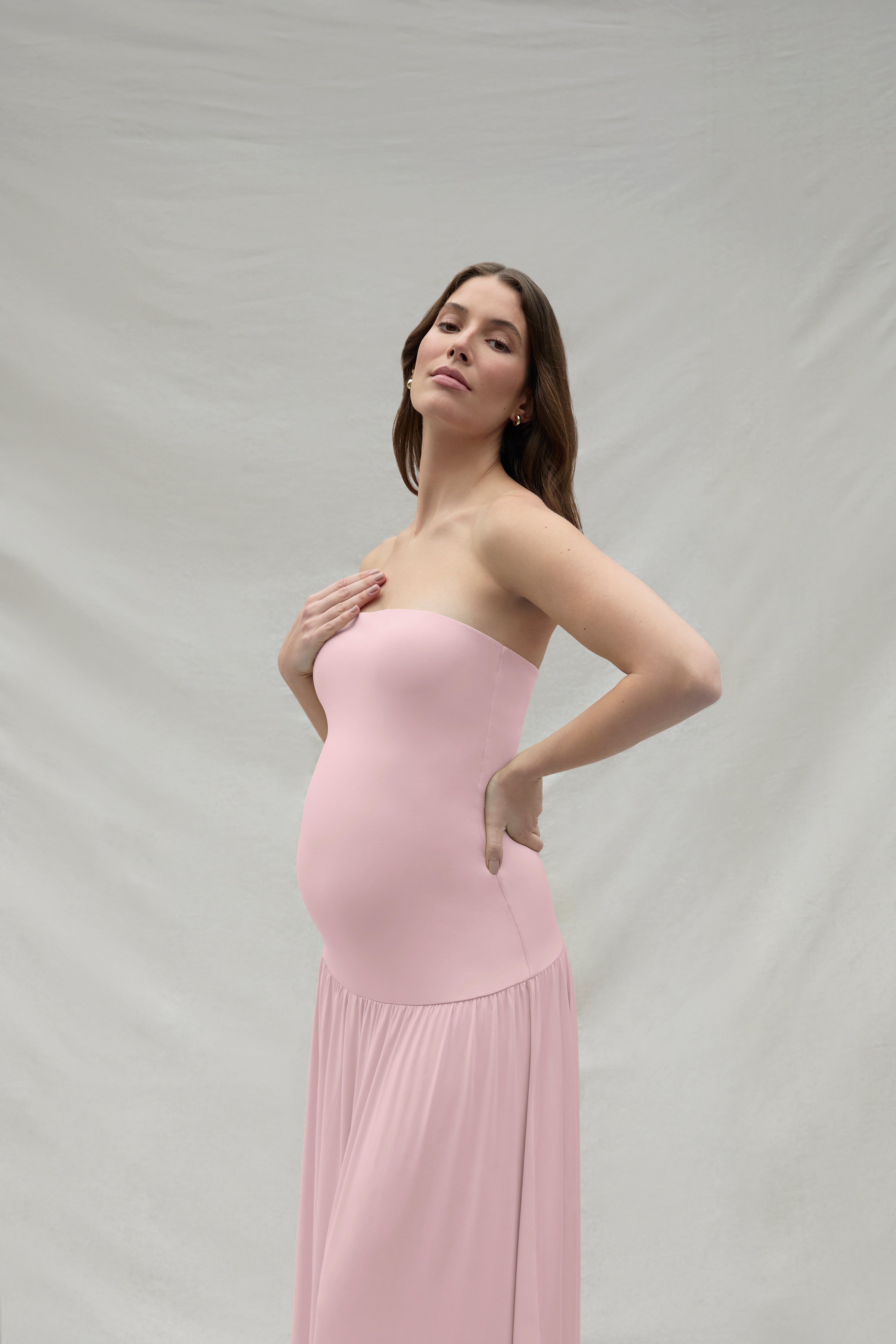 Woman wearing a pink strapless maternity dress against a plain background
