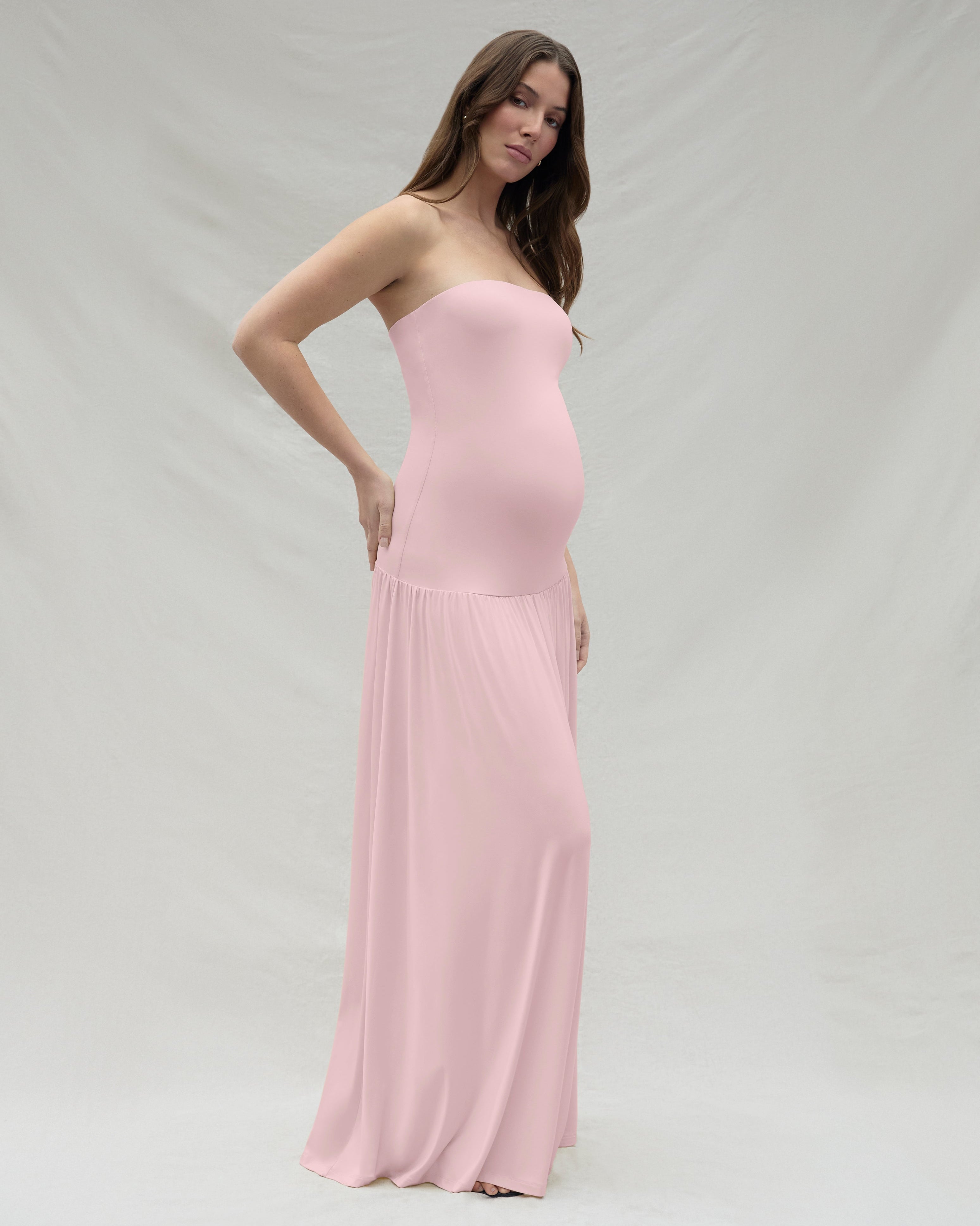 Woman wearing a strapless maternity pink dress against a plain background