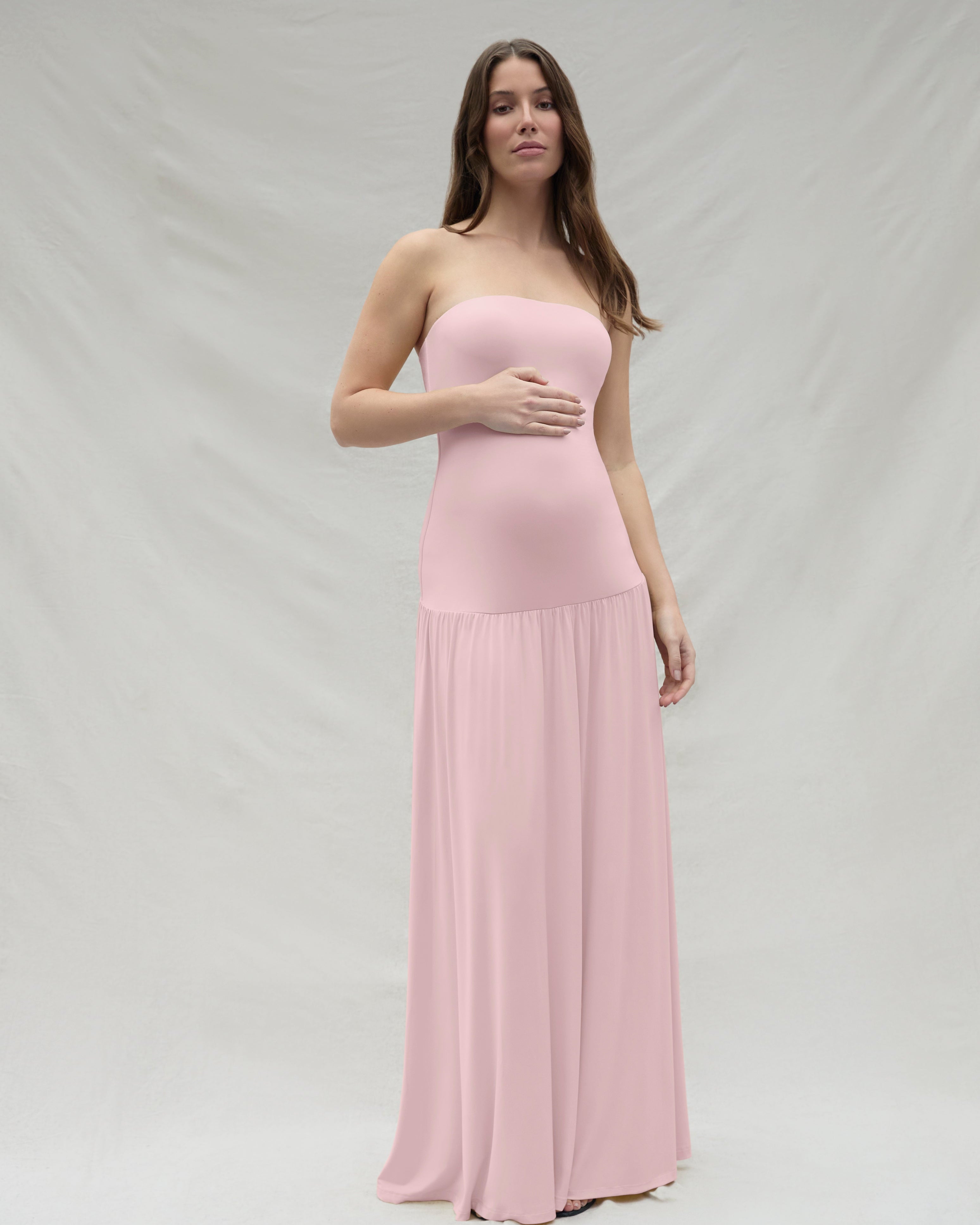 Woman wearing a pink strapless Bumpsuit gown against a white background