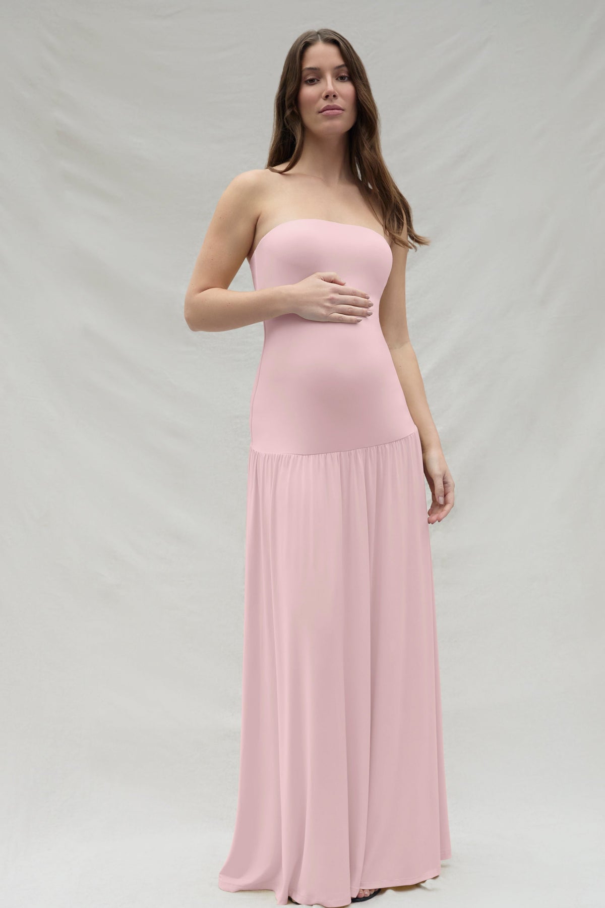 Woman wearing a pink strapless Bumpsuit gown against a white background