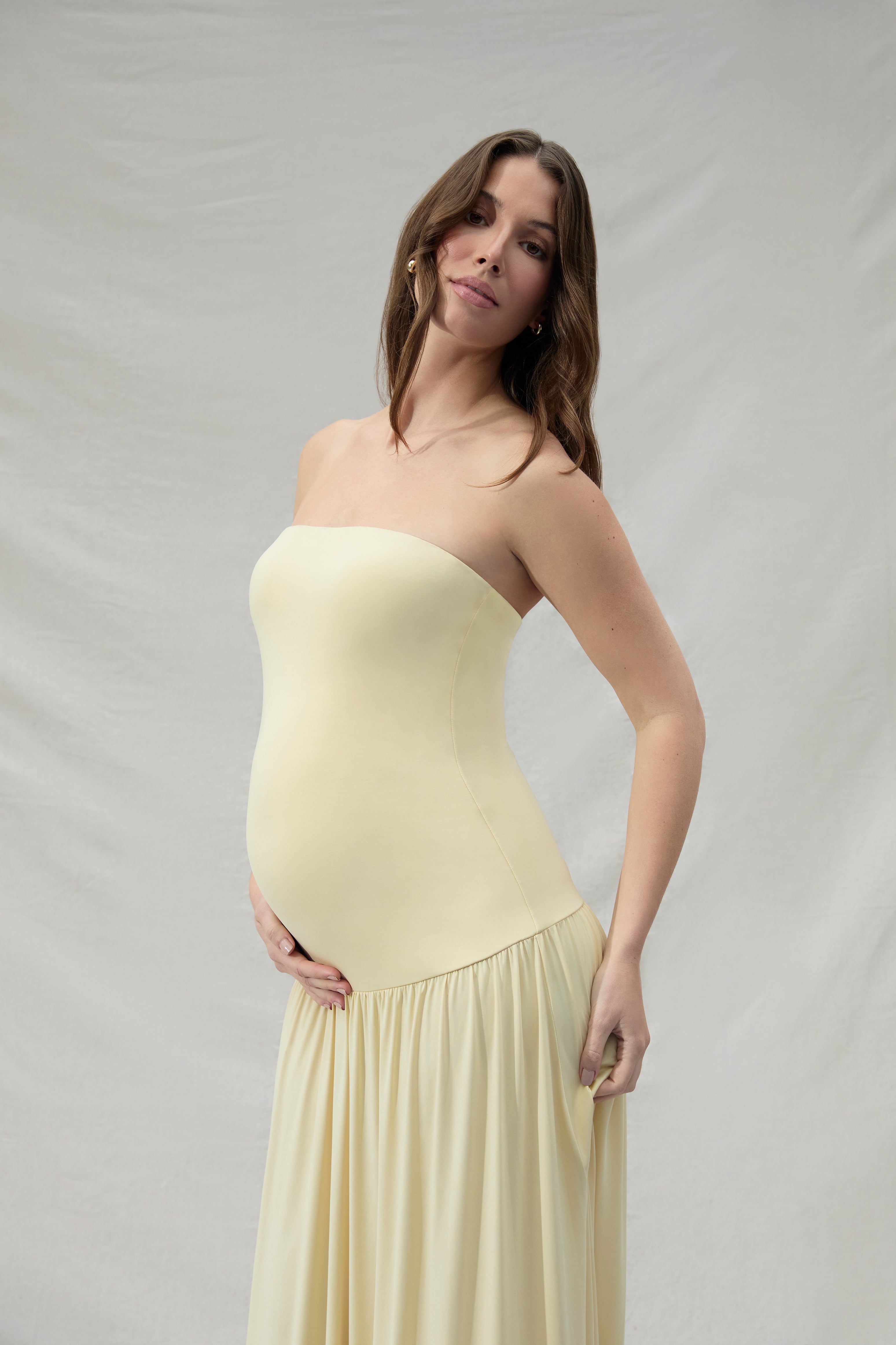 Pregnant woman wearing a maternity Bumpsuit strapless yellow dress against a plain background