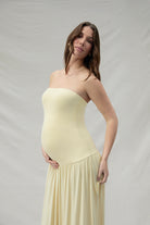 Pregnant woman wearing a maternity Bumpsuit strapless yellow dress against a plain background