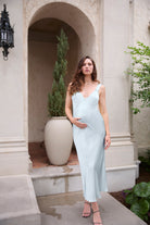 Woman in a light blue dress standing in an outdoor setting with architectural elements and plants.