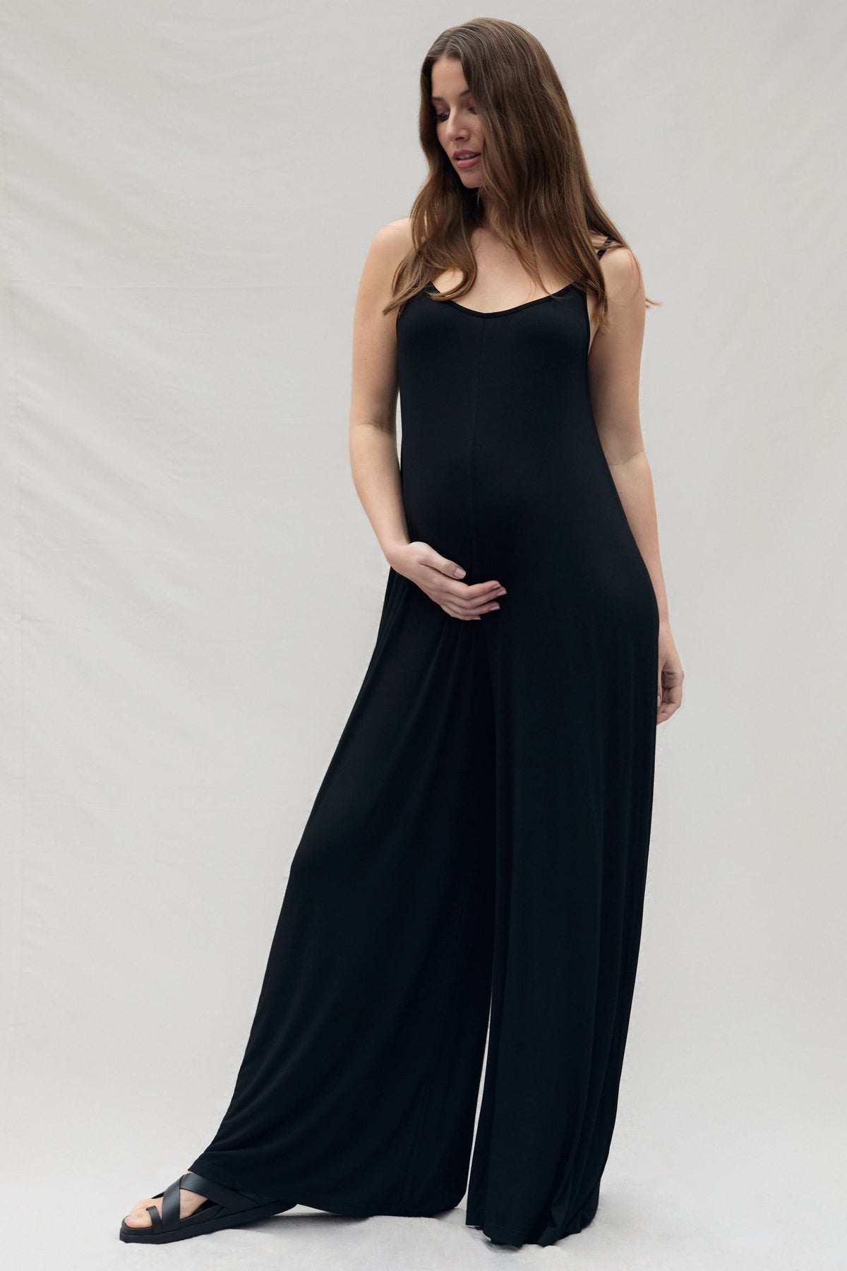 Pregnant woman wearing a black sleeveless cotton jumpsuit on a white background