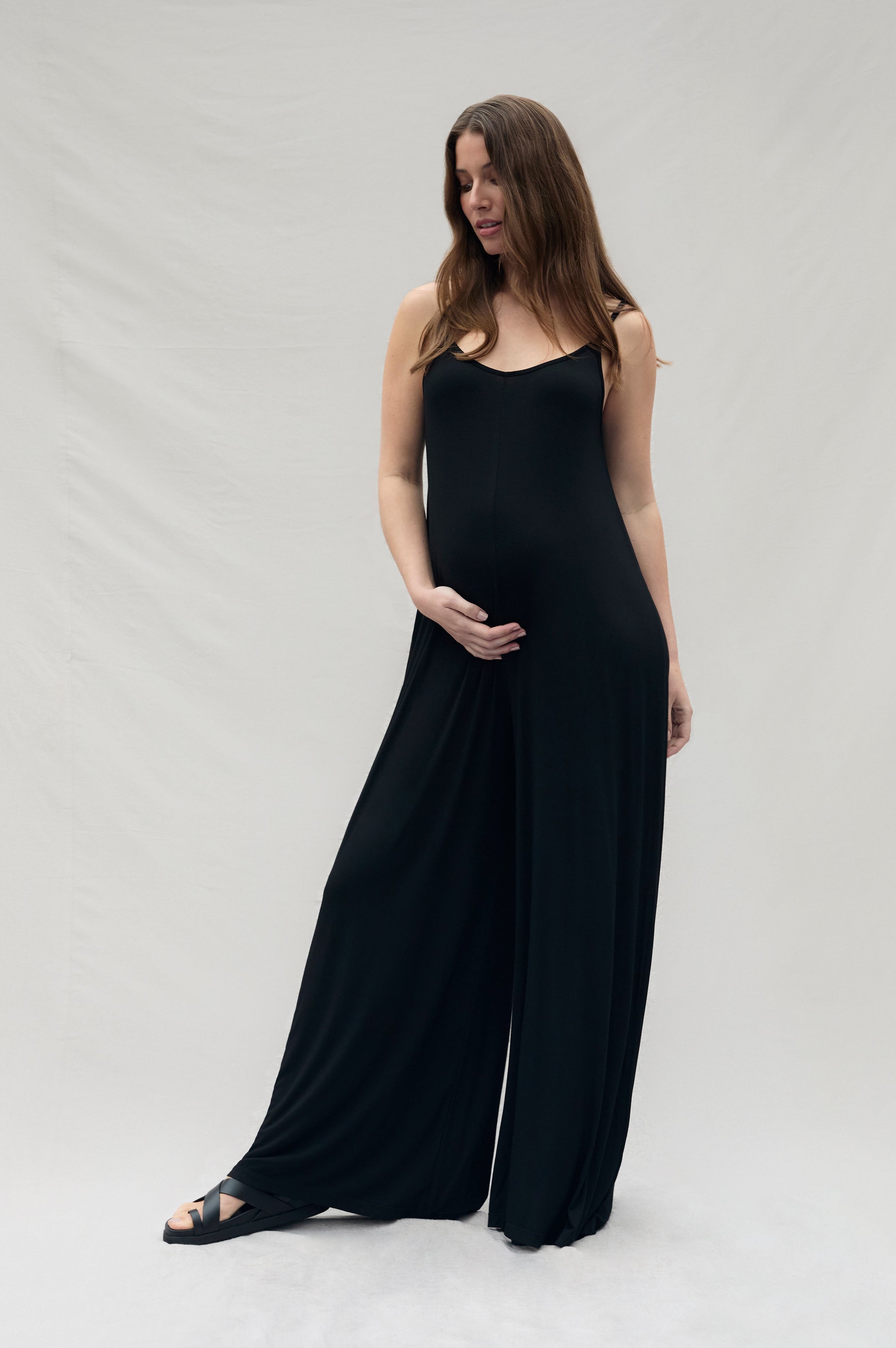 Pregnant woman wearing a black sleeveless cotton jumpsuit on a white background