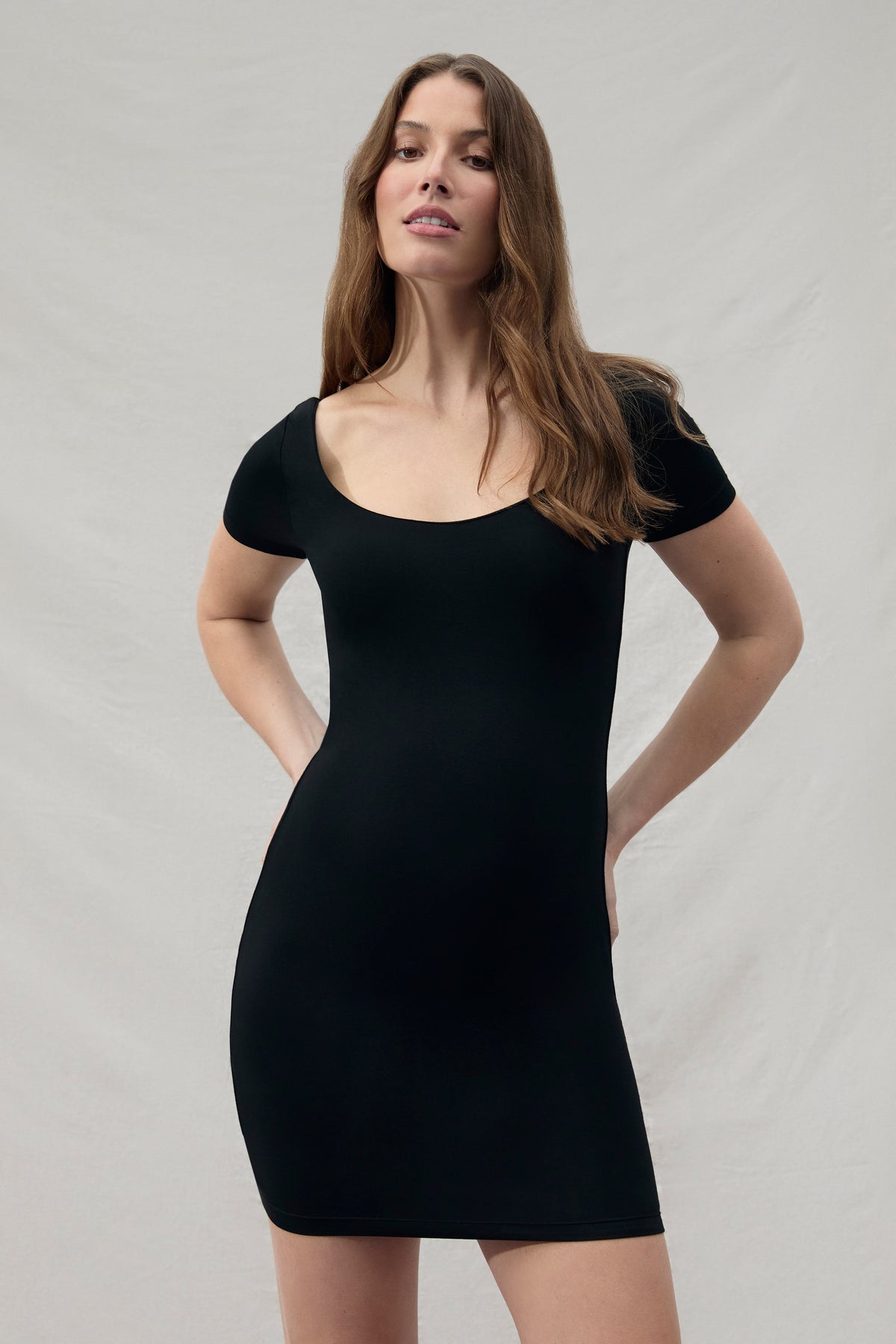 Woman wearing a mini black Bumpsuit dress against a plain background