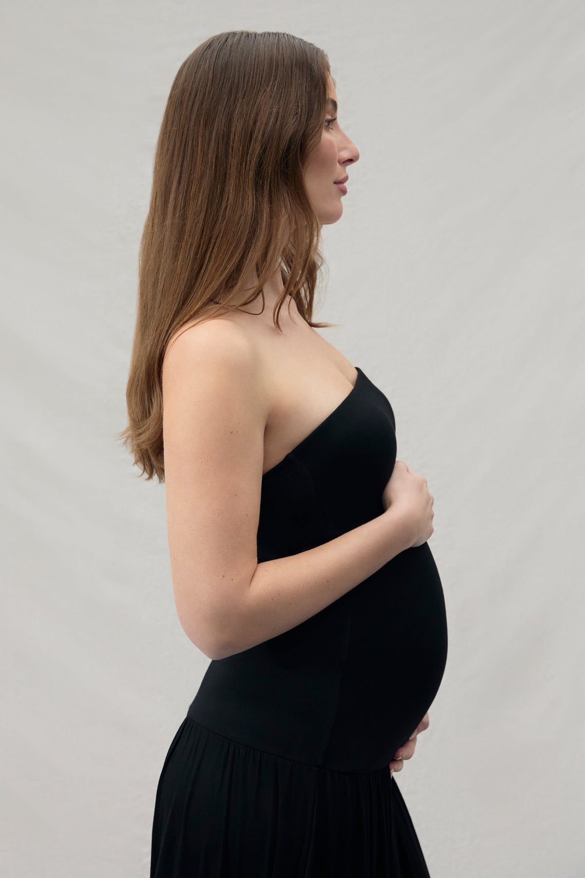 Pregnant woman wearing a black dress against a plain background