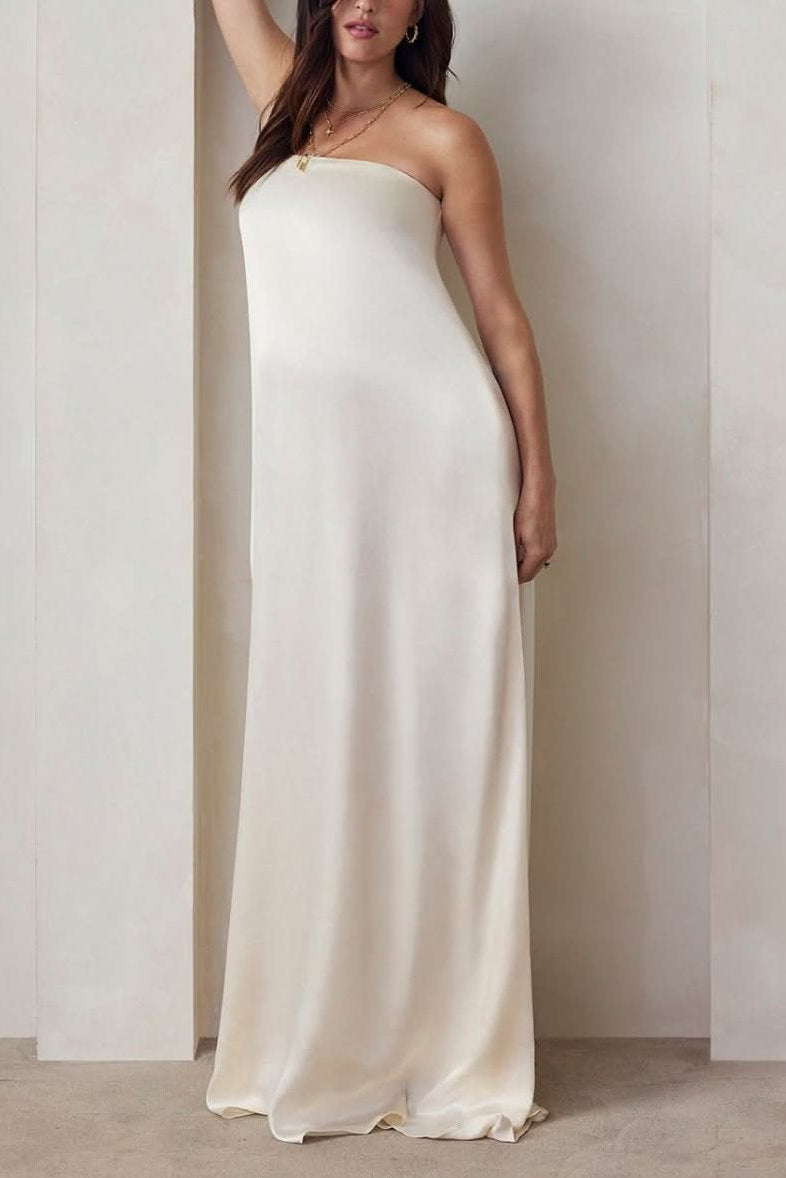 A Pregnant model wearing the Bumpsuit brushed satin gown in ivory against a beige feature wall.