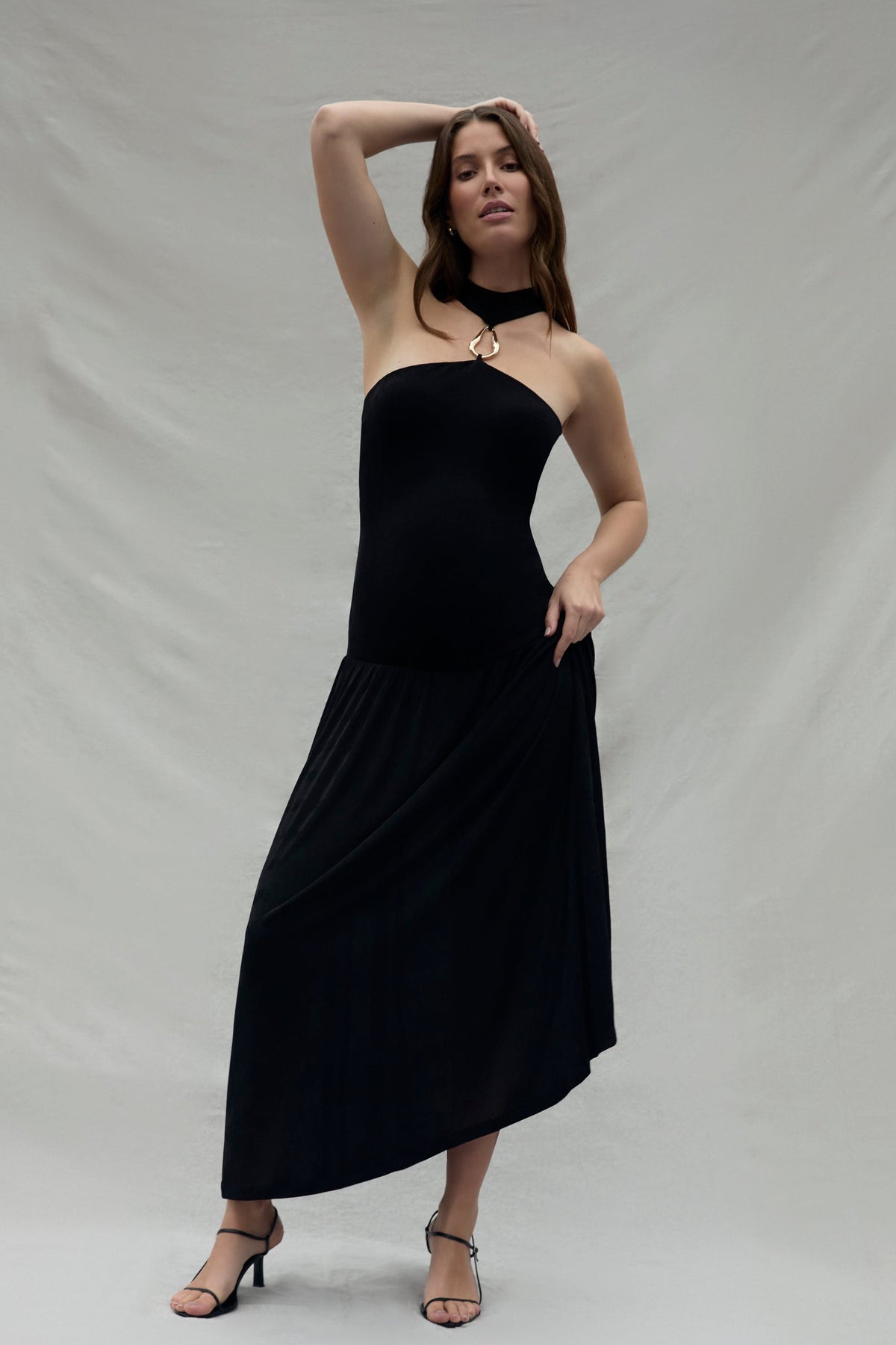 Pregnant woman wearing a black strapless halter dress with a gold halter accent against a plain background
