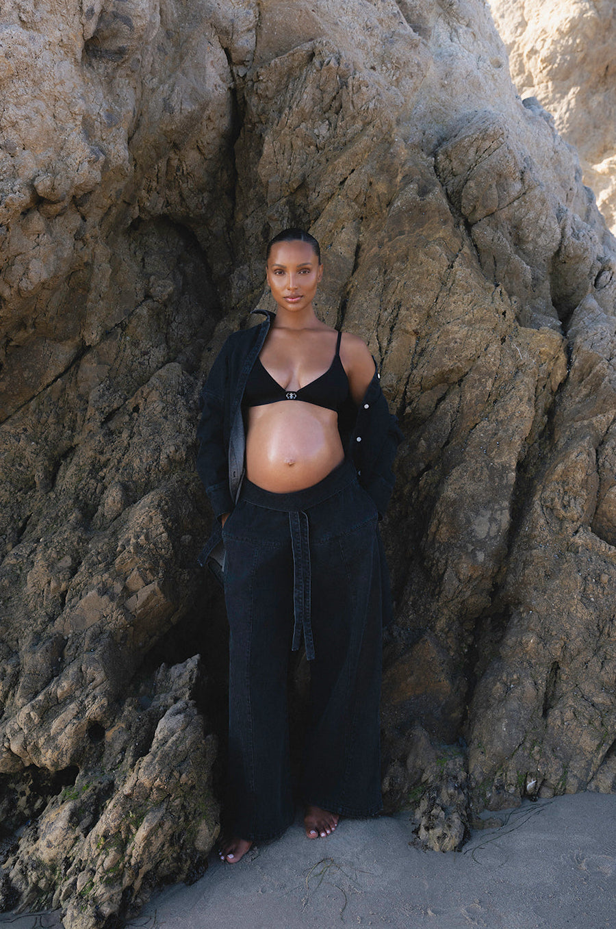 Pregnant woman in a black denim outfit standing against a rocky background