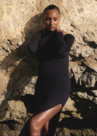 pregnant woman in a black Monica dress standing against a rocky wall
