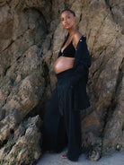 Pregnant woman in black denim Bumpsuit outfit standing against a rocky wall