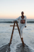 jasmine tookes standing on a ladder in the ocean wearing bumsuits maternity luxe pjs
