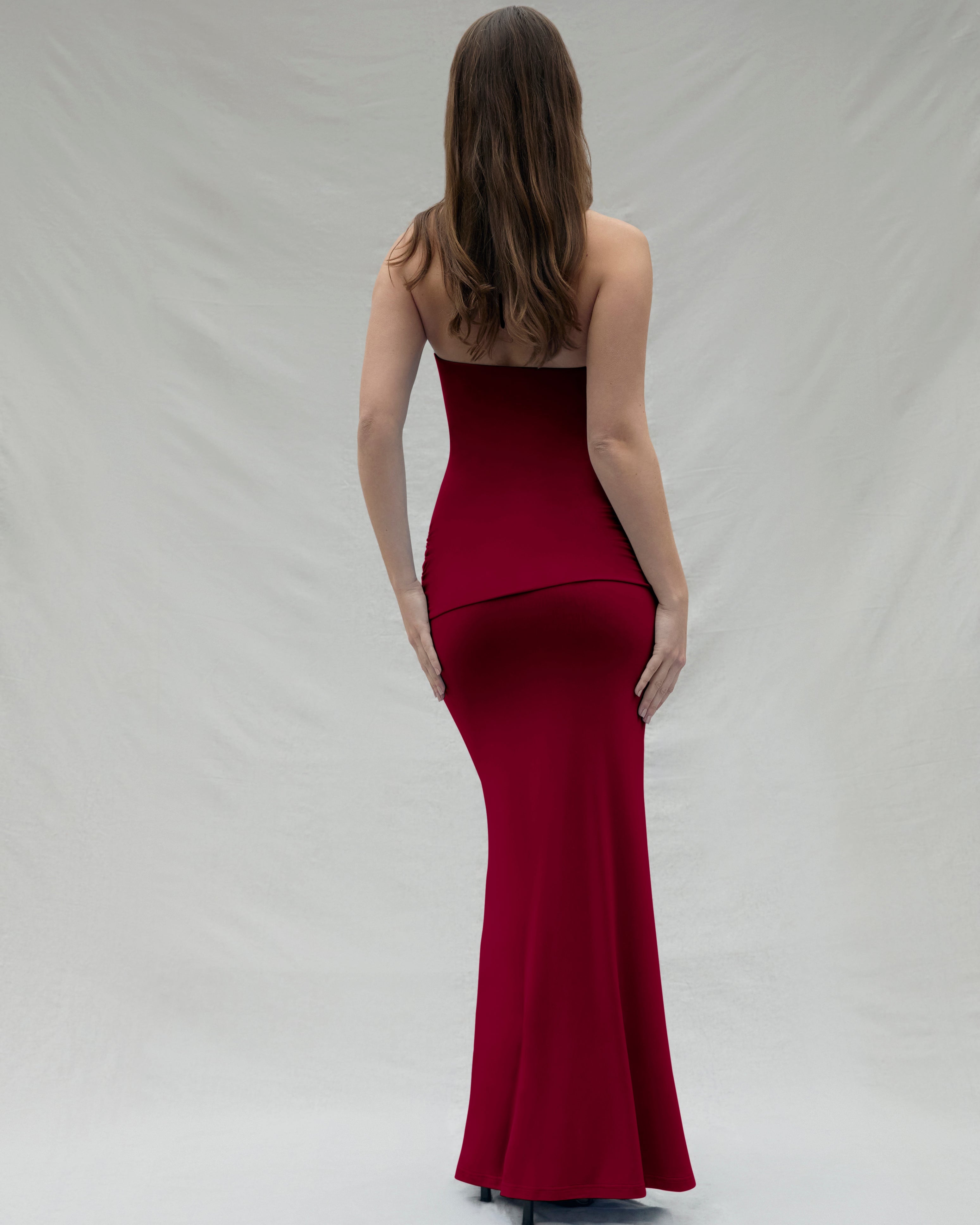 backview of a woman wearing a burgundy maxi Bumpsuit dress on a white background