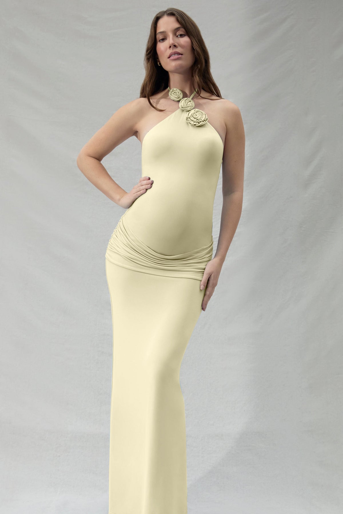 Pregnant woman wearing a light yellow floral halter neck dress against a plain background