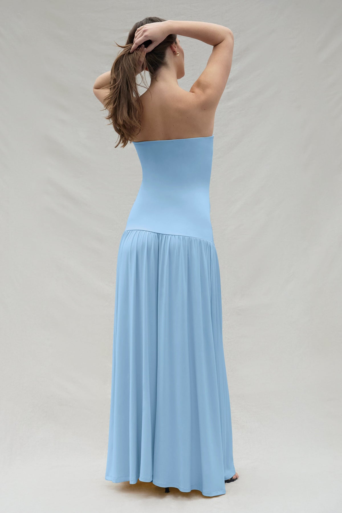 Back view of a woman wearing a powder blue strapless gown against a plain background